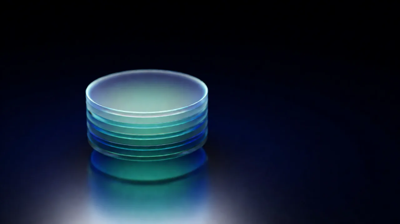 A stack of translucent glass discs glowing teal and blue above a dark reflective surface