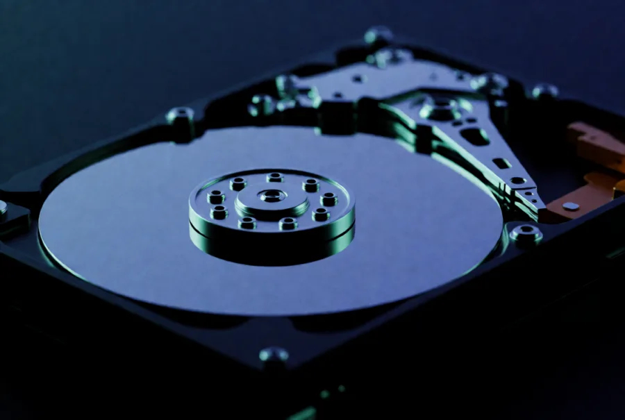 An opened hard drive with its mirror-polished platter exposed, lit in teal and blue